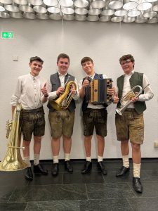 Jugendliche Musiker in Tracht mit Instrumenten vor moderner Wandverkleidung