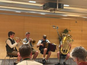 Blasmusikgruppe spielt in Tracht im Festsaal, vier Musiker mit Trompete, Flügelhorn, Ziehharmonika und Tuba.