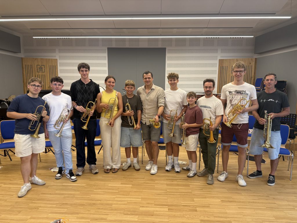 Blechbläserensemble mit zehn Mitgliedern und ihren Instrumenten in einem Proberaum